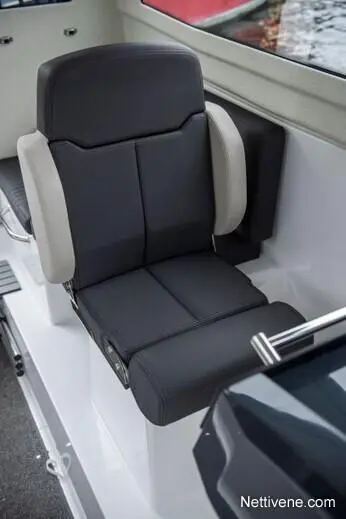 A black and gray marine boat seat with armrests, located indoors near a window overlooking water.